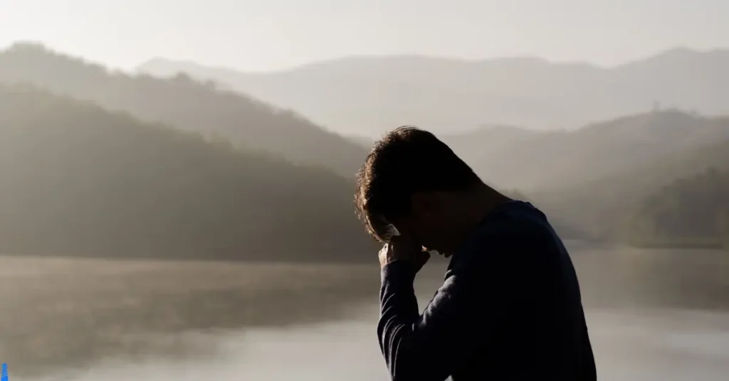 Picture of a person holding their head by a foggy mountain lake.