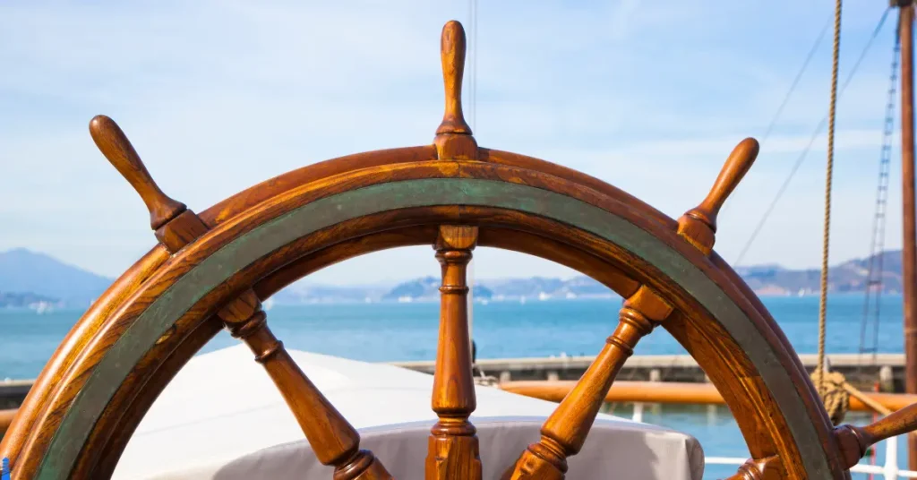 A ship's wheel with the sea and shore in the background.