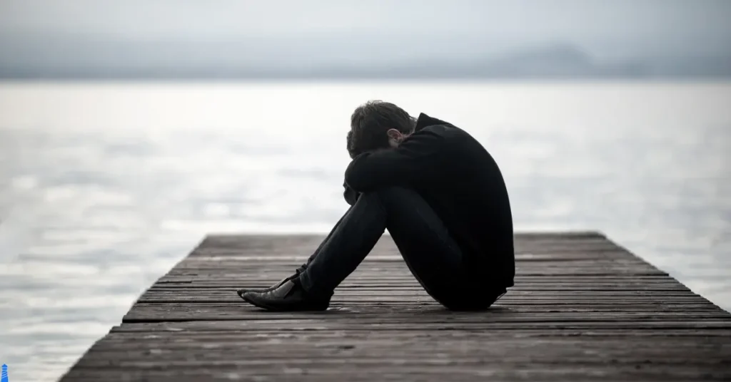 Man on a dock, sitting on a dock, hands in face, unhappy.