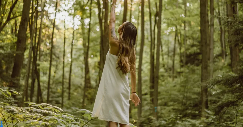 A woman in a white dress walking in the woods.