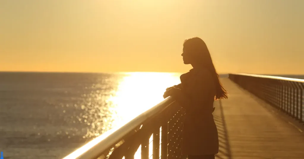 Woman alone on a pier at sunrise looking into the distance.