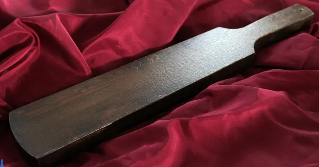 Spanking paddle made of dark wood on a deep red background.