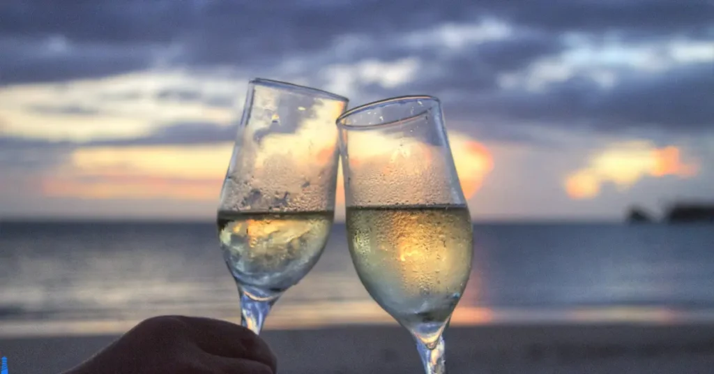 Two chilled classes with condensation clinking together in a toast at sunset on a beach.