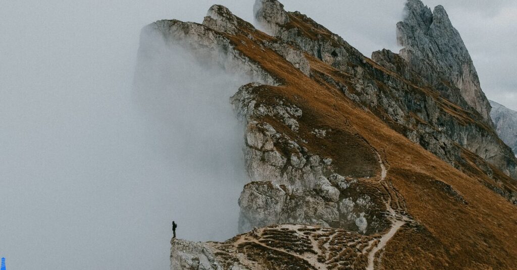 Hiker standing on the edge of a cliff with mist swirling around.