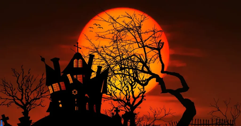 A haunted looking house with leafless trees and a setting orange sun behind.