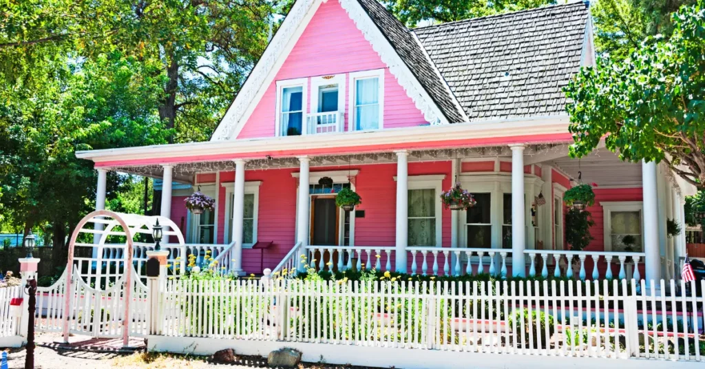 Pink farm house with a wrap around porch.