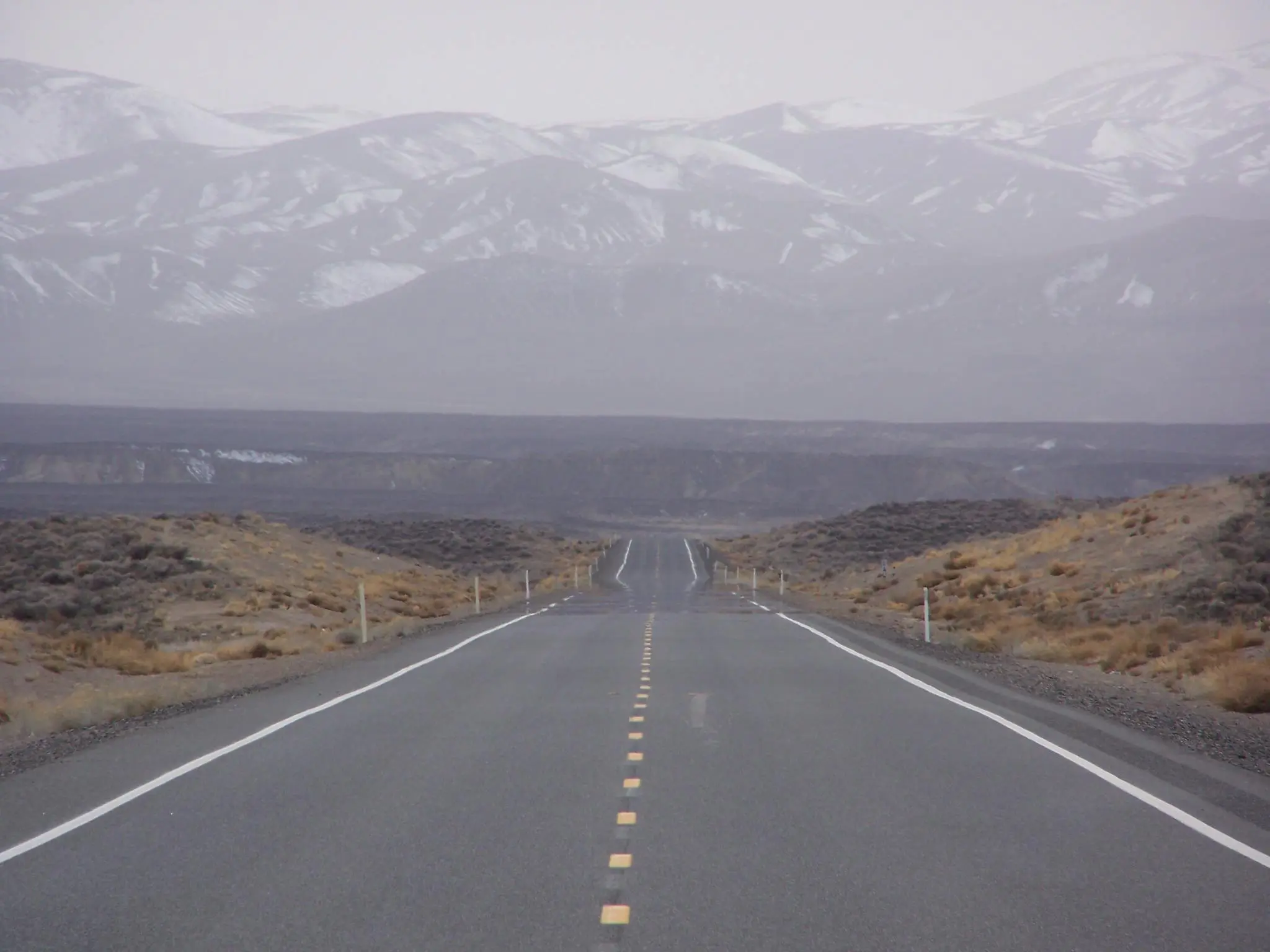 U.S. 50, the loneliest road in America, Nevada. Empty road with snow capped mountains.