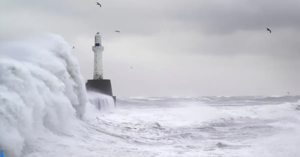 A lighthouse about to be hit by a massive wave.